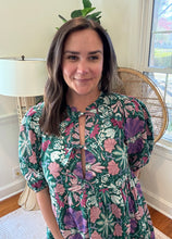 Load image into Gallery viewer, Green and purple floral printed mini dress. Puff sleeves, triple front closure, babydoll style with pockets. Light weight cotton and lined. Personally did not need tank under ties, but could be worn.
True to size, wearing size small.
Good for bump, post bump or no bump.
Step into whimsical elegance with this green and purple floral printed mini dress, perfect for breezy days and effortless style. Designed in a flattering babydoll silhouette, this dress features puff sleeves for a romantic touch and