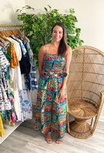 Load image into Gallery viewer, Sefina jumpsuit in paradiso print. Light weight cotton with straight pants and smocked bodice. Adjustable straps and removable tie at waist - could add a straw belt. Hits at ankle length for flats as well.  True to size. Wearing size small, but would take x-small for a more fitted look.
