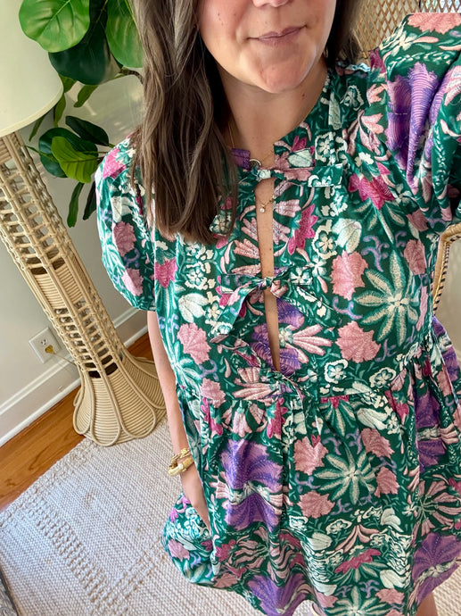 Green and purple floral printed mini dress. Puff sleeves, triple front closure, babydoll style with pockets. Light weight cotton and lined. Personally did not need tank under ties, but could be worn.

True to size, wearing size small.

Good for bump, post bump or no bump. 

Step into whimsical elegance with this green and purple floral printed mini dress, perfect for breezy days and effortless style. Designed in a flattering babydoll silhouette, this dress features puff sleeves for a romantic touch and