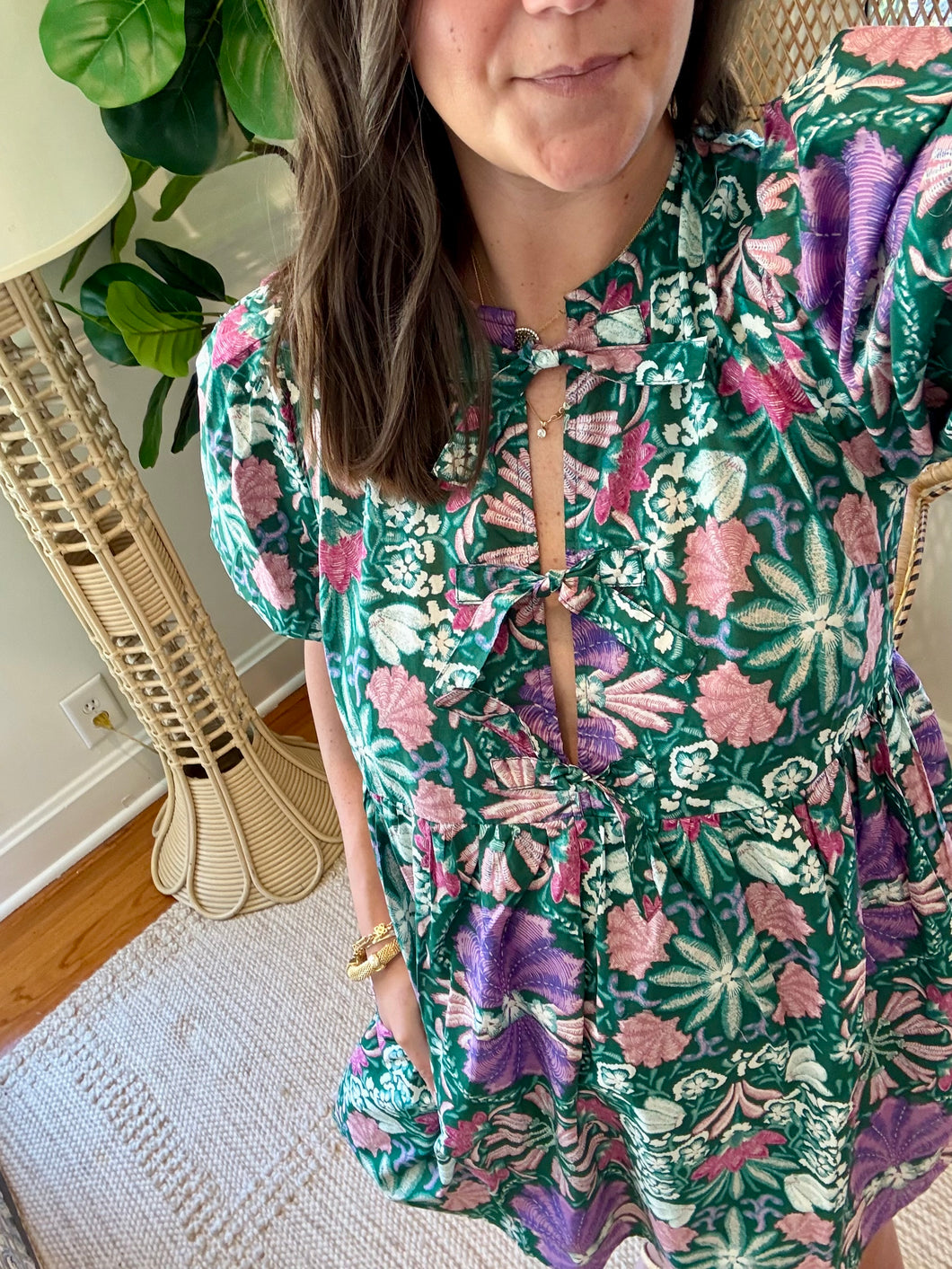 Green and purple floral printed mini dress. Puff sleeves, triple front closure, babydoll style with pockets. Light weight cotton and lined. Personally did not need tank under ties, but could be worn.

True to size, wearing size small.

Good for bump, post bump or no bump. 

Step into whimsical elegance with this green and purple floral printed mini dress, perfect for breezy days and effortless style. Designed in a flattering babydoll silhouette, this dress features puff sleeves for a romantic touch and