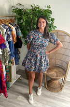 Load image into Gallery viewer, Navy floral print mini dress with bubble hem and bubble sleeves. Smocking cinched at waistline. Small open back with tie closure at top, bra friendly. Poly cotton blend.  True to size, wearing size small.
