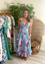 Load image into Gallery viewer, Blue and pink floral ankle dress with ruffle asymmetric skirt. Pleated shell bodice and belt with straw buckle. Adjustable straps, smocked backside and side zipper closure.  If between sizes, size up. Wearing size small.
